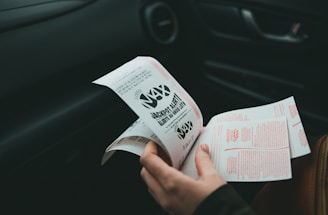 A person is holding and examining what appears to be lottery tickets inside a car. The image is focused on the tickets and the person's hands, with parts of the car interior visible in the background.